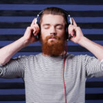 Music lover. Confident young bearded man in headphones standing against stripped background and listening to the music